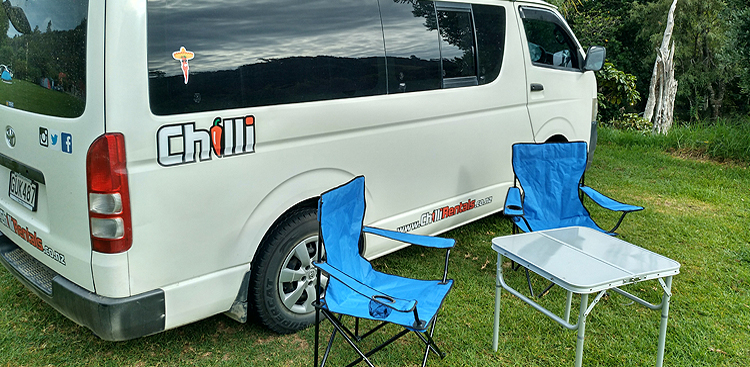 Campingtisch und Stühle neben dem Trustee Traveller Camper von Chilli Rentals in Neuseeland