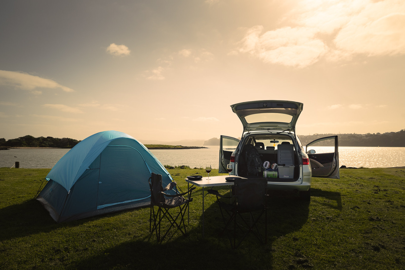 Budget Camper mit geöffneter Heckklappe und Zelt am Meer in Neuseeland
